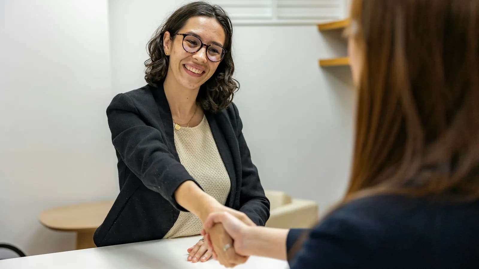 Two women shaking hands across a table after a job interview